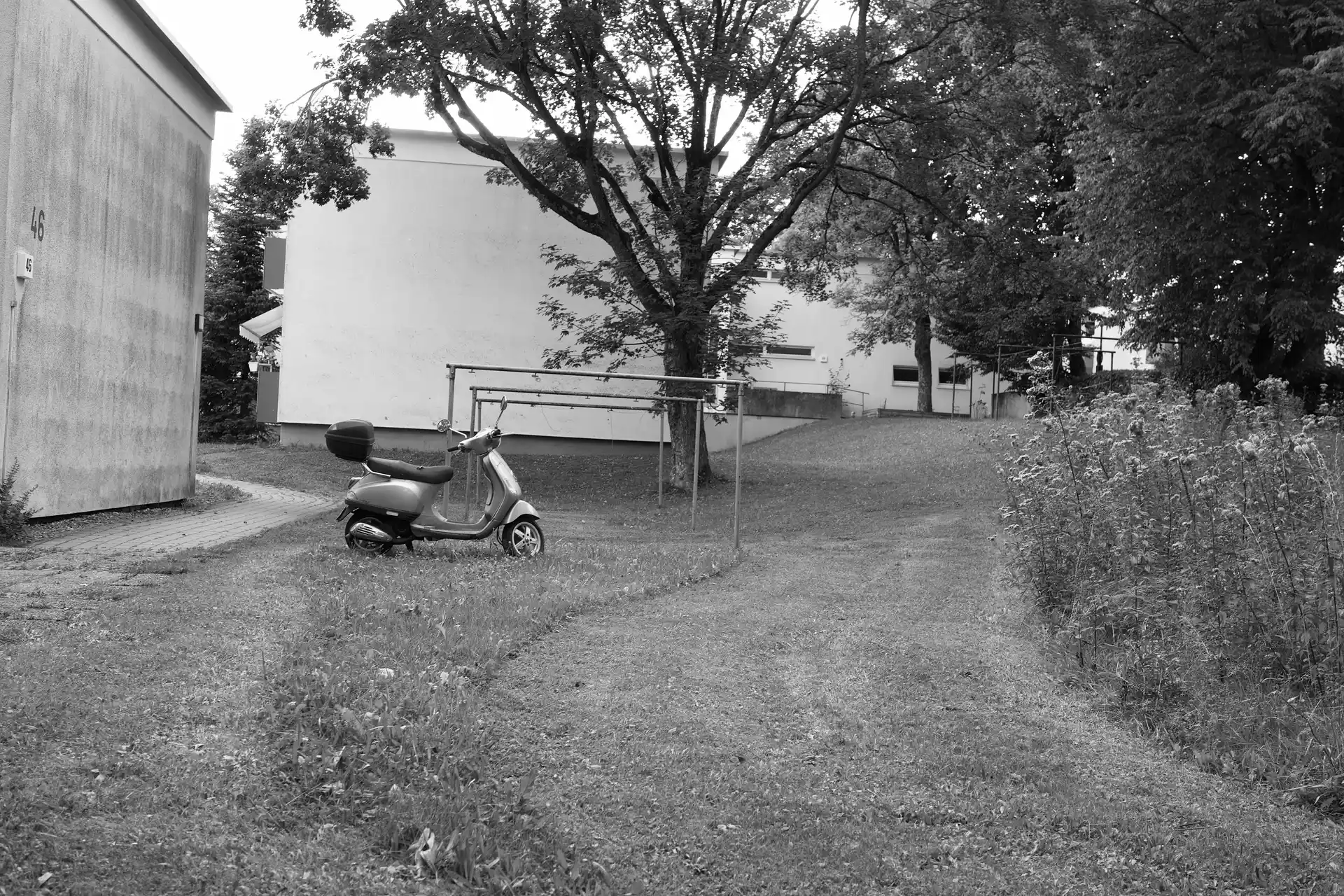 A classic looking scooter parked next to a outdoor clothes rack on a lawn. The lawn was mowed around the vehicle.