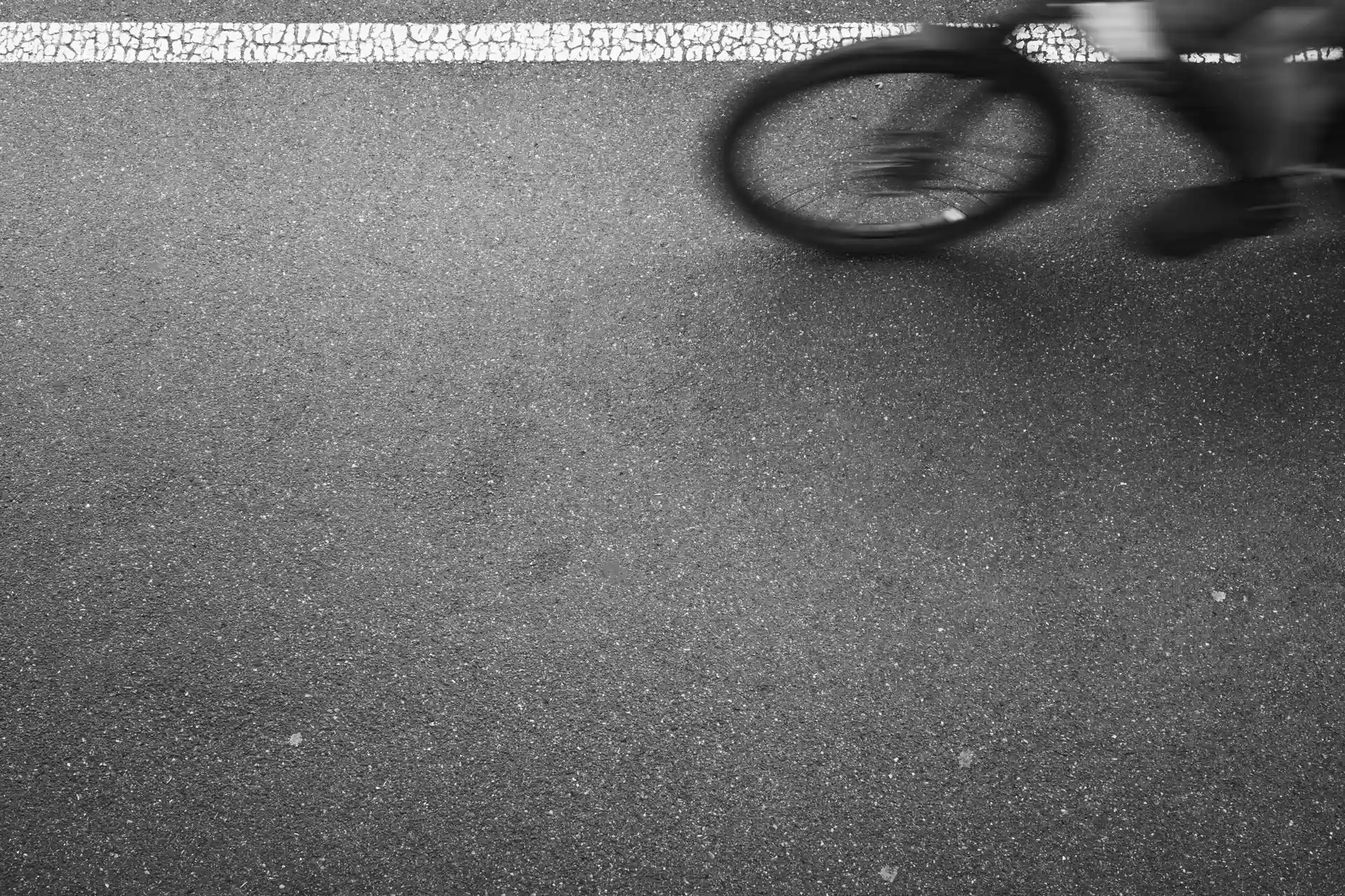 A part bicycle of a bicycle in motion in front of a horizontal white line on the asphalt.