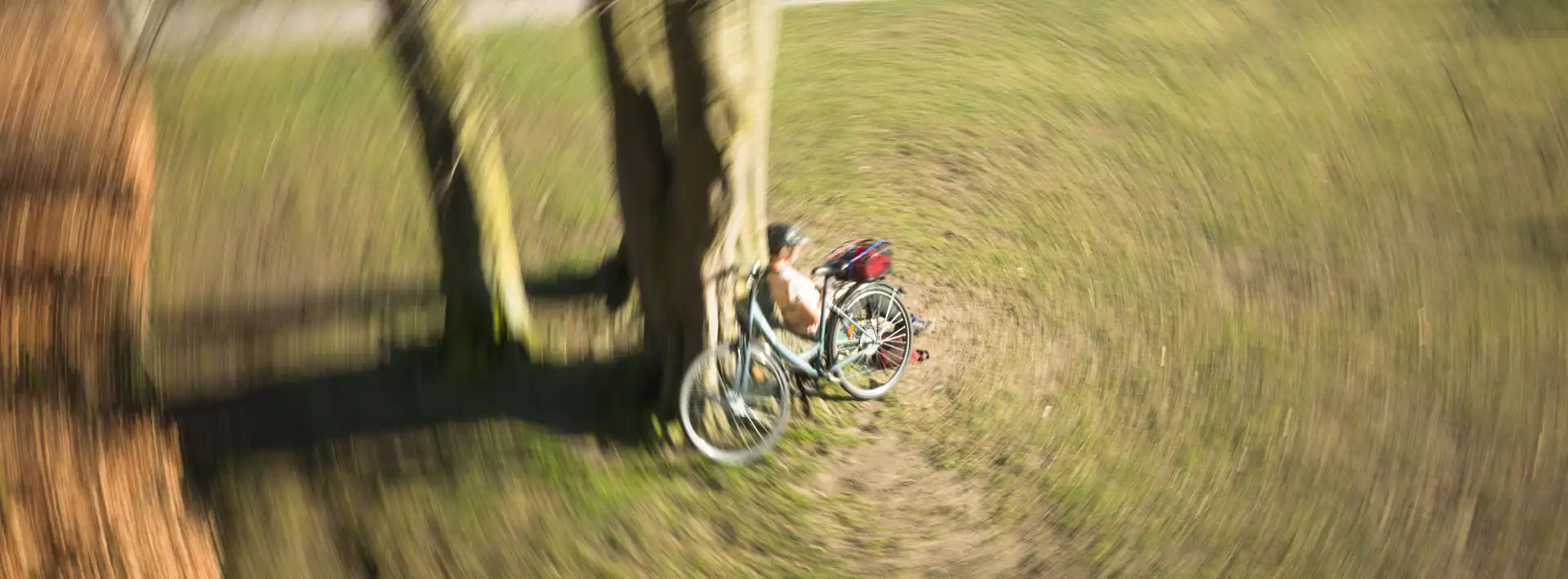 Picture of a person with they're bicycle sitting at a tree. The camera was rotated during exposure resulting in a circular effect.
