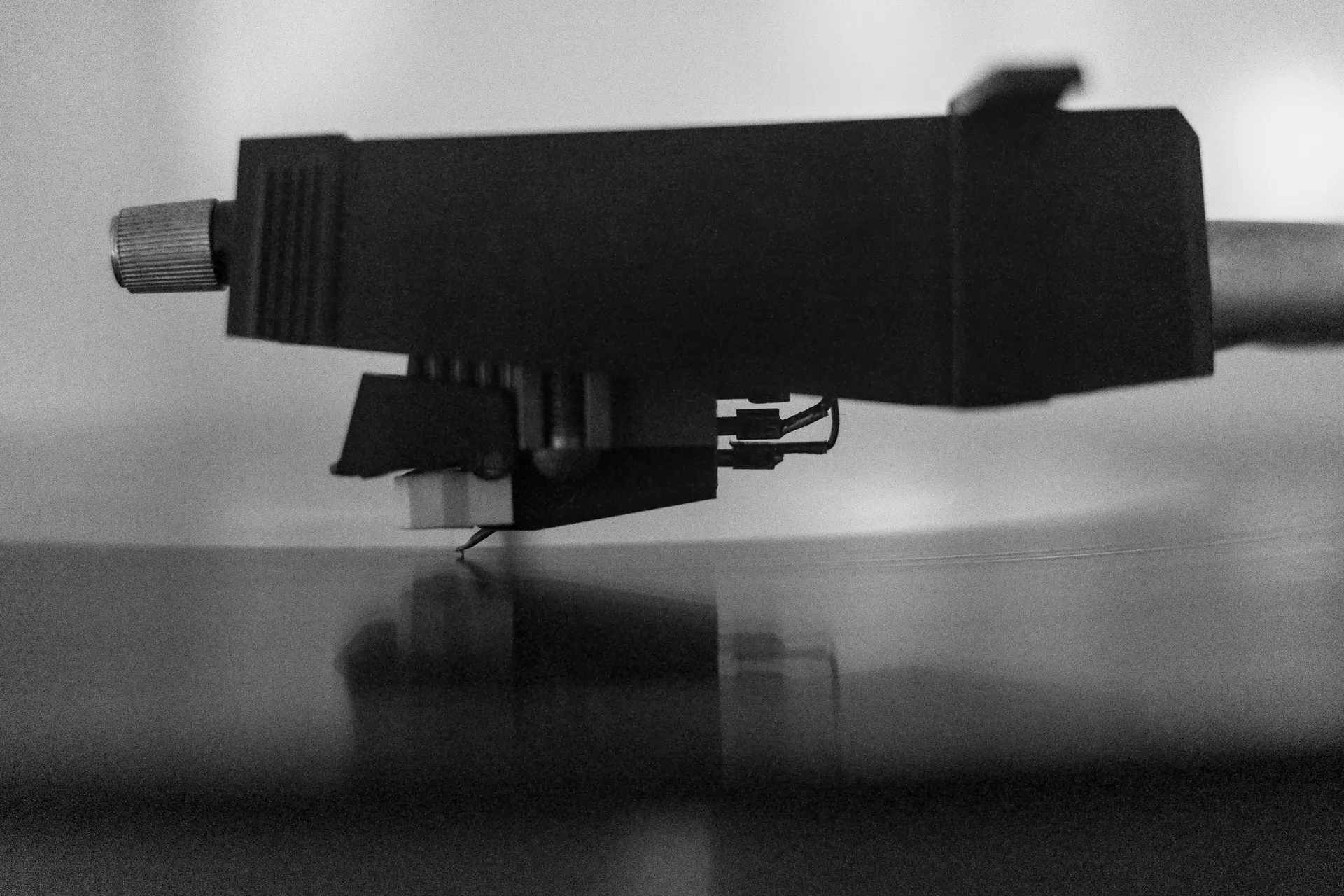 Close-up photo of the cartridge of a turntable while playing a record. The cartridge is partly mirrored in the vinyl.